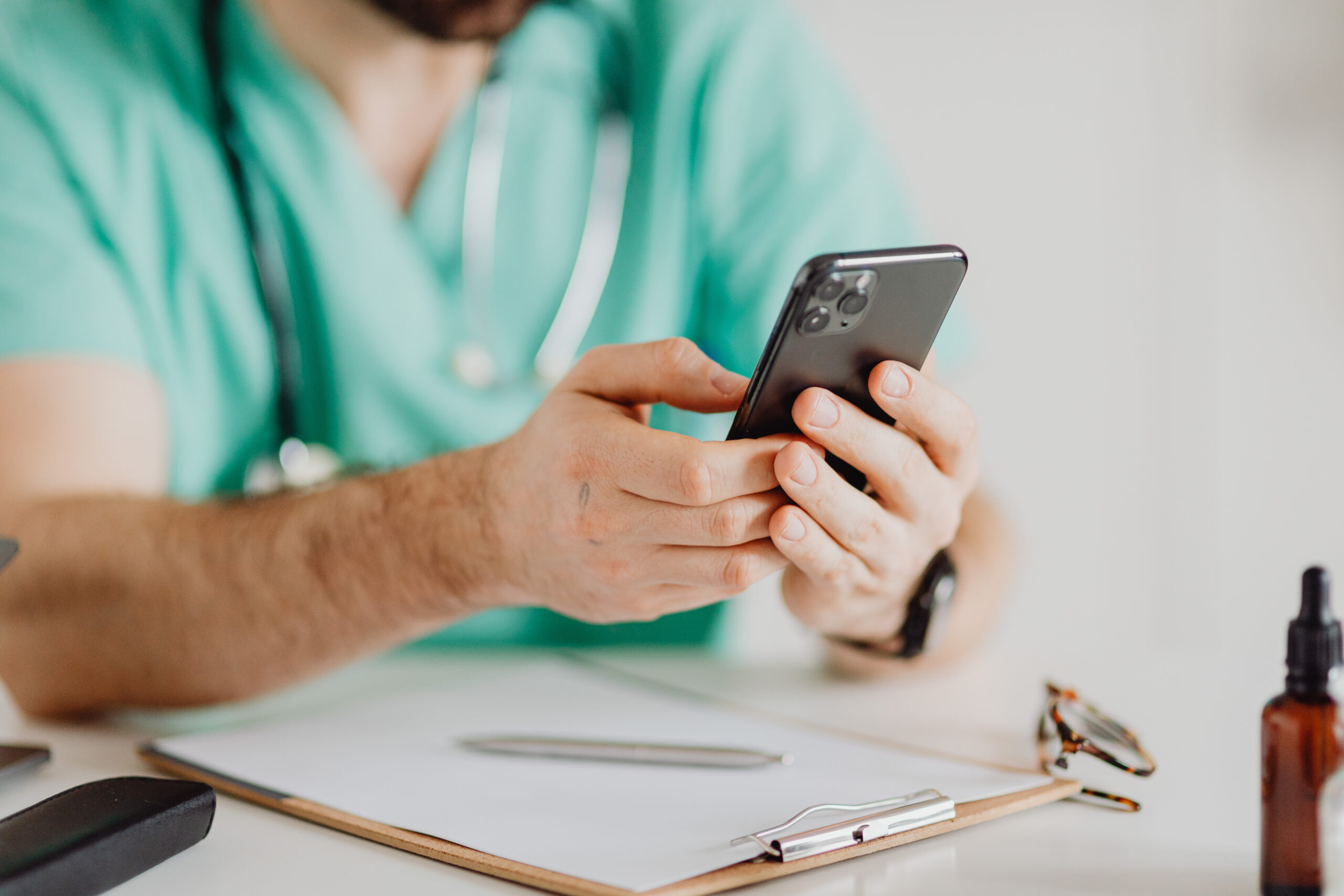 happy-male-doctor-sitting-his-office-communicating-with-someone-mobile-phone
