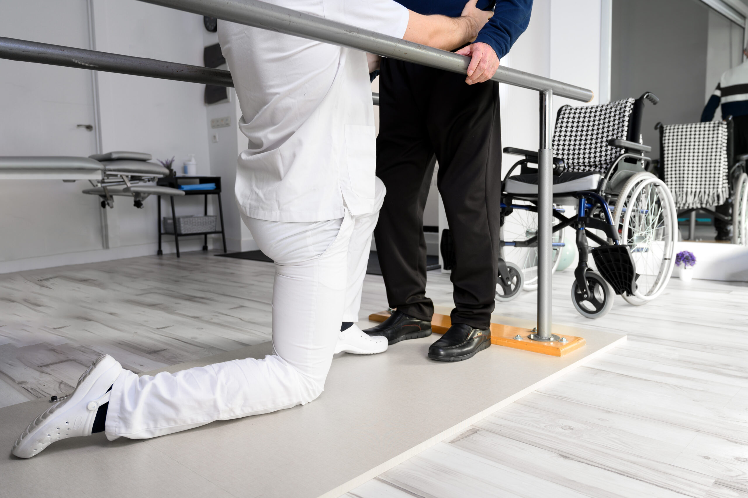 Physiotherapist helping disabled Caucasian senior man to walk with parallel bars in rehabilitation center